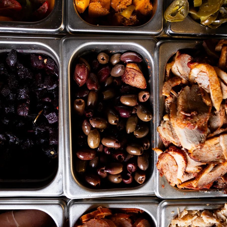 Trays of olives, pulled meat and roast vegetables on the topping bench