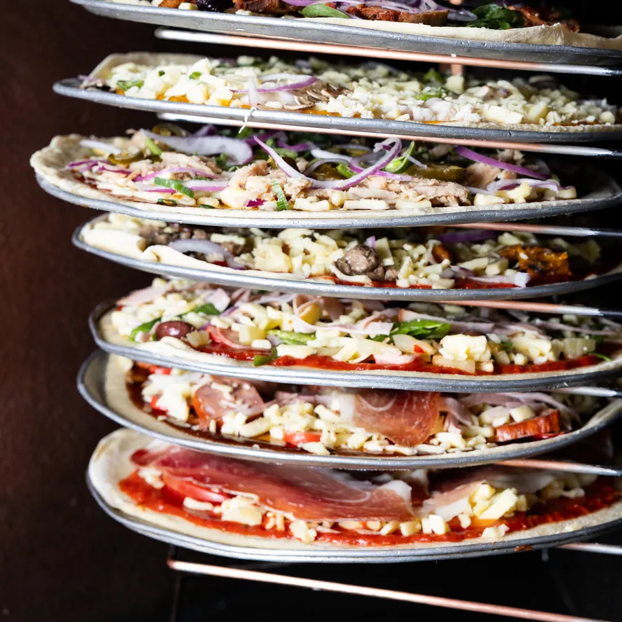 A rack of topped pizzas on trays, waiting for the oven