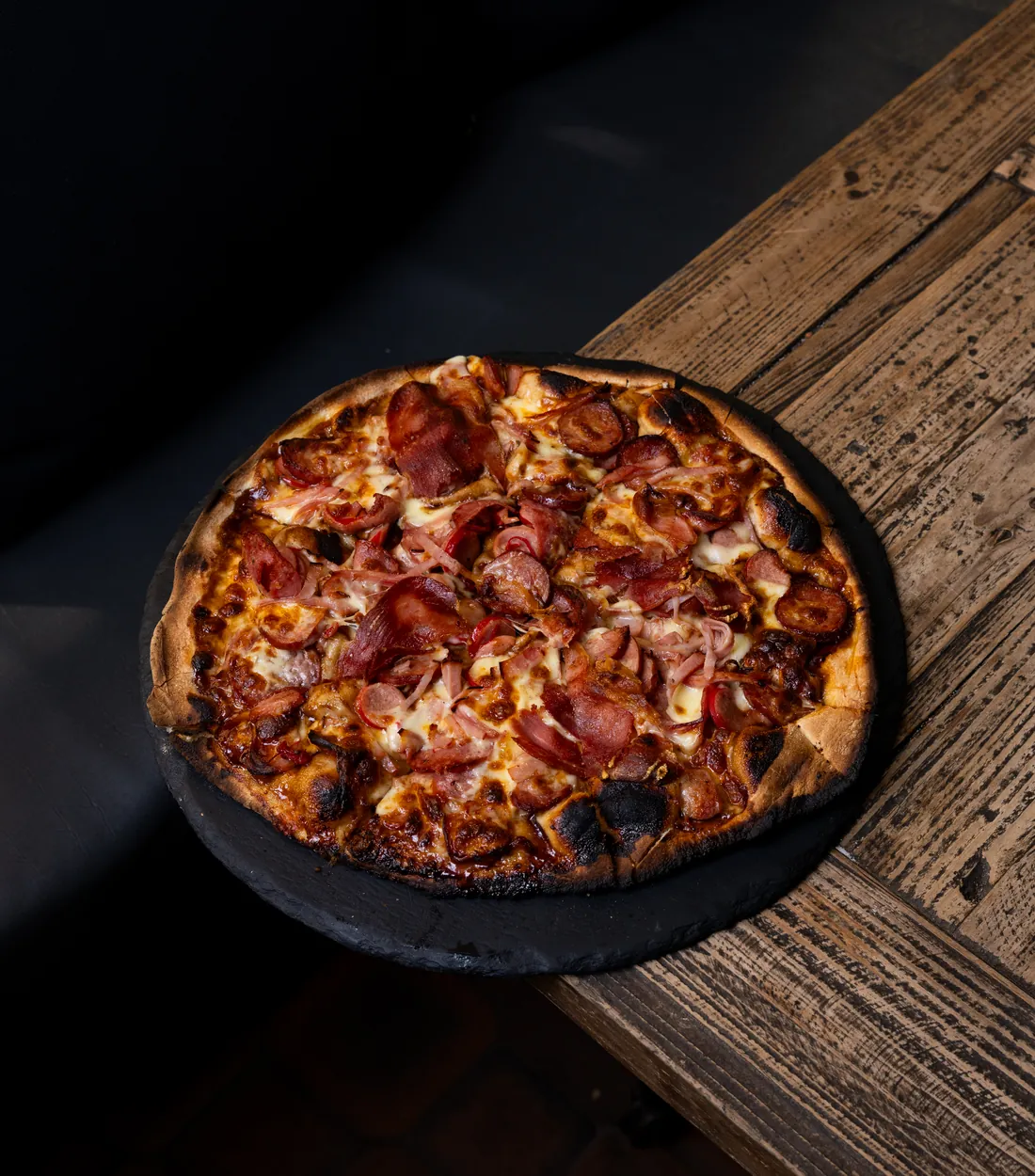 A woodfired ham and salami pizza on a slate board