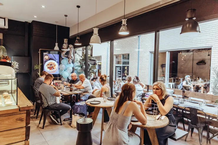Guests talking over drinks at round tables in the front dining room