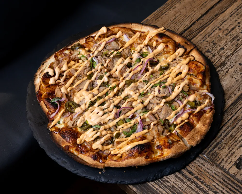 A woodfired pizza drizzled with aioli on a slate board