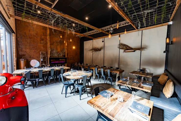 The dining room laid with timber tables and blue-grey chairs under hanging greenery, a red Vespa in the corner