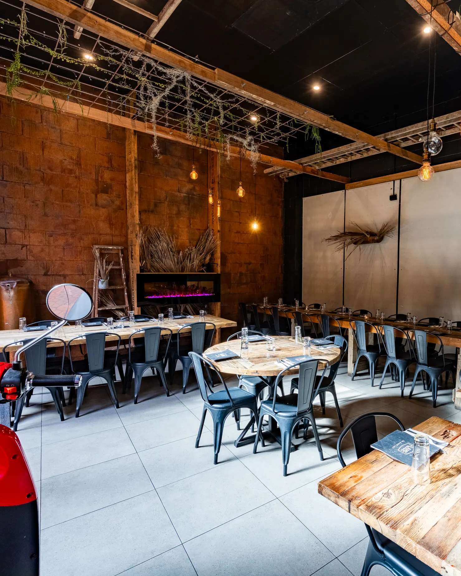 The dining room set for service, with timber tables, metal chairs, pendant lights and a brick wall