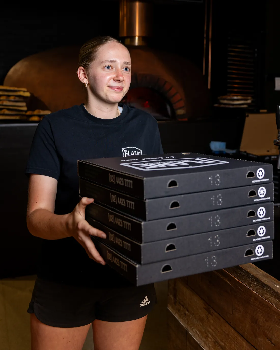 A staff member carrying a stack of five Flame pizza boxes