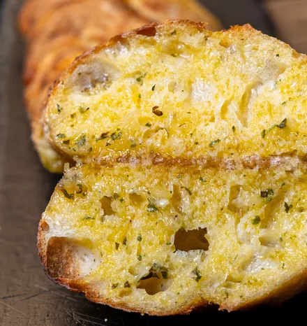 A garlic loaf cut open to show its buttery herb-flecked crumb