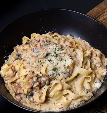 Creamy fettuccine with mushrooms and grated parmesan in a black bowl